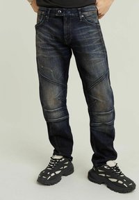 Tmavě modré džíny slim fit s ostrými švy a jemným vyblednutím, doplněné černými sportovními botami.