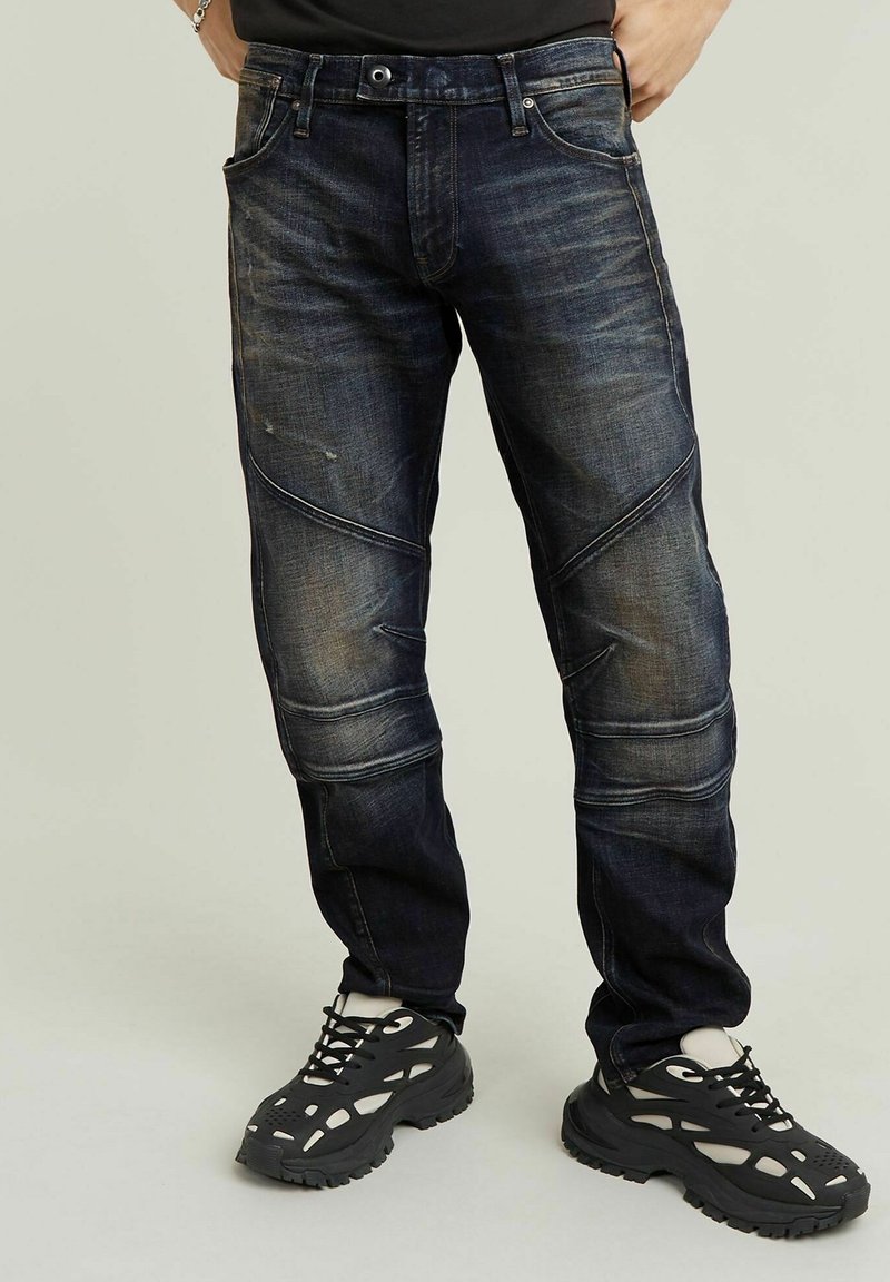 Tmavě modré džíny slim fit s ostrými švy a jemným vyblednutím, doplněné černými sportovními botami.