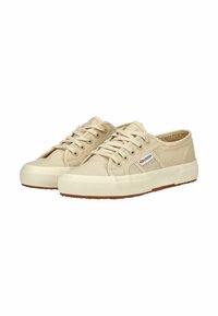 Zapatillas de lona en beige claro con suela de goma, punta redonda y diseño con cordones; cuenta con una pequeña etiqueta de la marca en el costado.