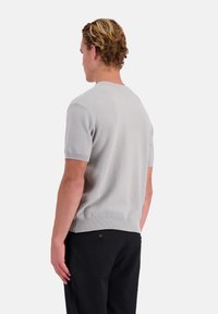 Lichtgrijze korte mouwen gebreide trui met een gestructureerd patroon en een geribbelde zoom, gecombineerd met zwarte broek. Zicht vanaf de achterkant.