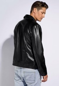 Schwarze Leder-Motorradjacke mit glatter Textur, urbanem Kragen und Reißverschlussmanschetten, kombiniert mit hellblauen Jeans.