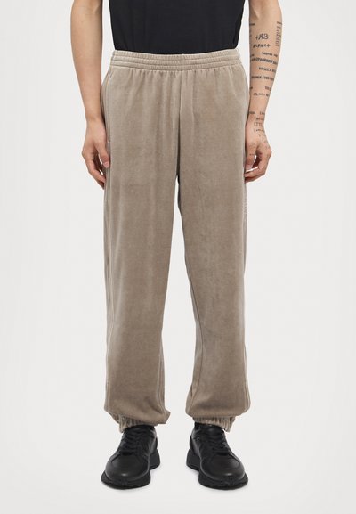 Beige fleece joggers with an elastic waistband, side pockets, and elastic cuffs. Worn with black athletic shoes.
