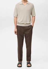 Polo à manches courtes beige clair avec une texture côtelée ; associé à un pantalon sur mesure brun foncé et des sandales noires à semelle plate.