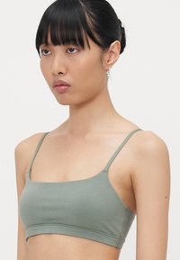 Hellgrüne Stretch-Baumwoll-Bralette mit dünnen verstellbaren Trägern und rechteckigem Ausschnitt. Glatte Textur, minimale Nähte, lässiges Design.