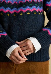 Námornícky pletený sveter s farebným zigzag vzorom v ružovej, zelenej, fialovej a žltej farbe, s rebrovanými manžetami a mäkkou textúrou.