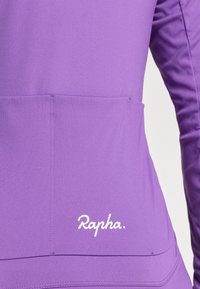 Camisa de mangas longas roxa, feita de um tecido suave, com um bolso nas costas e um logo branco "Rapha" perto da bainha.