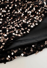 Tissu noir ornée de sequins roses dorés brillants et denses. La doublure intérieure est lisse, noire avec une couture visible le long du bord.