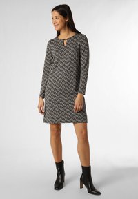 Schwarz-weißen gemusterte Kleid mit langen Ärmeln, rundem Ausschnitt und einem Schlüssel-Ausschnitt, gerade Silhouette, kombiniert mit schwarzen Knöchelstiefeln.