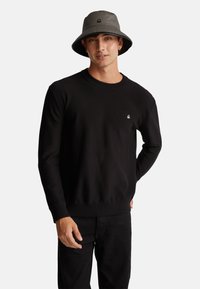 Maglione a maglia nera con scollatura rotonda e orlo a costine, abbinato a pantaloni neri. Presenta un piccolo logo bianco sul petto.