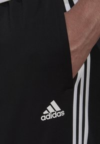 Schwarze Sportshorts mit einem weißen Dreistreifen-Design entlang der Seiten. Mit einem Adidas-Logo auf der unteren linken Seite. Hergestellt aus strukturiertem Stoff.