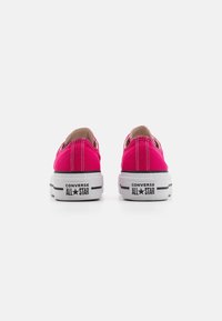 Sneaker in tela rosa brillante con suole in gomma bianca, dettagli neri e un logo sul tallone, caratterizzate da un design a taglio basso e dettagli cuciti.