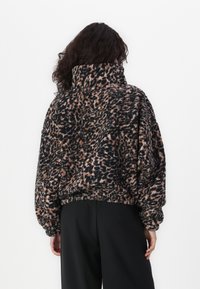 Pullover de forro polar suave con estampado de leopardo, de cuello alto, corte holgado y mangas caídas. Los colores incluyen negro, marrón claro y acentos en rosa apagado.