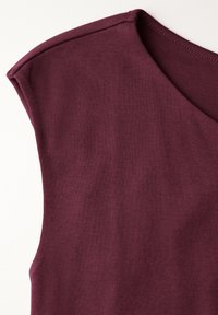Burgundská bezrukávová košile vyrobená z jemné látky, s výstřihem ve tvaru V a jemným šitím kolem okrajů. Hladký povrch s přiléhavým střihem.