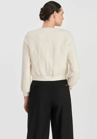 Teksturowany kremowy sweter z okrągłym dekoltem i prążkowanym dołem. Połączony z czarnymi spodniami, które podkreślają dopasowaną talię i szerokie nogawki.