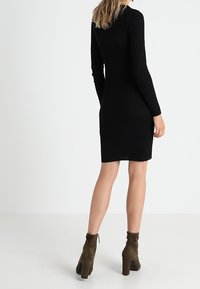 Robe noire en tricot à manches longues, texture côtelée, longueur au genou, associée à des bottines à talons hauts couleur vert olive.