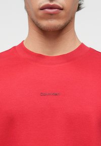 Czerwona bawełniana bluza z okrągłym dekoltem, z subtelnym szarym logo "Calvin Klein" z przodu, gładka struktura i regularny krój.