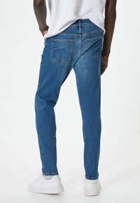 Vaqueros de denim azul ajustados con un acabado ligeramente desgastado, cinco bolsillos y un diseño de pierna recta. Combinados con zapatillas blancas.