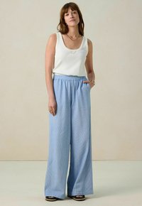 Lichtblauwe, wijde broek met een gestructureerde stof en een elastische tailleband. Gecombineerd met een strak wit tanktop.