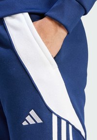 Marineblauwe trainingbroek met witte zijstrepen, een zijzak en een gestructureerde afwerking. Bevat een drie-strepenlogo op de bovenbeen.