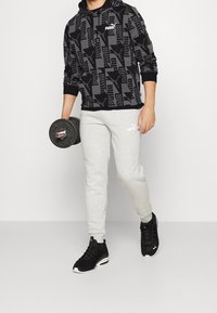 Sweat à capuche noir à motif avec cordon de serrage, pantalon de survêtement gris et baskets noires. Le pantalon arbore un logo ; le sweat présente un design texturé.