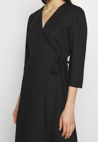 Schwarzes Wickelkleid mit V-Ausschnitt, dreiviertel Ärmeln und einem Bindeband in der Taille, aus einem glatten Stoff gefertigt. Schlichtes und elegantes Design.