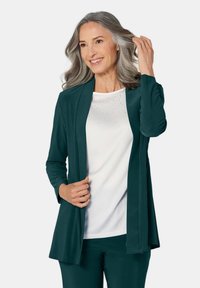 Teal lange mouwen open-front cardigan over een witte top met verspreide rhinestones. De stof lijkt zacht; gelaagd met een ontspannen pasvorm.