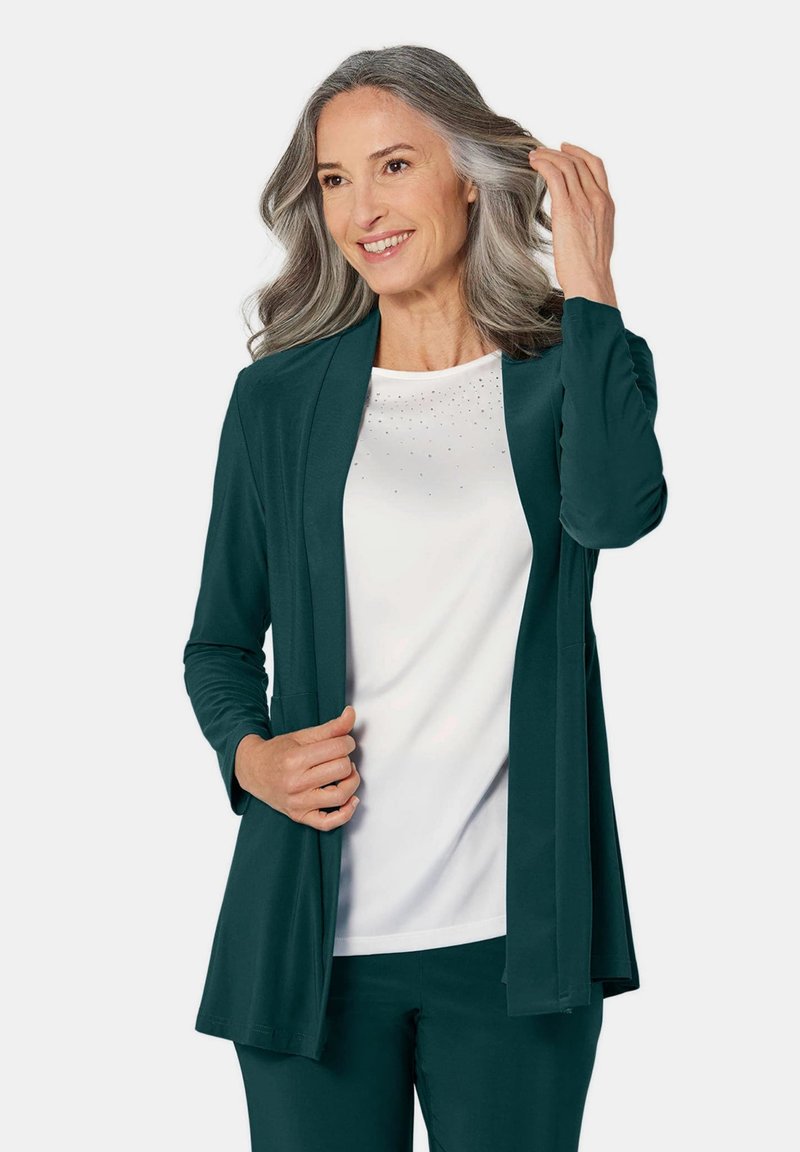 Teal lange mouwen open-front cardigan over een witte top met verspreide rhinestones. De stof lijkt zacht; gelaagd met een ontspannen pasvorm.