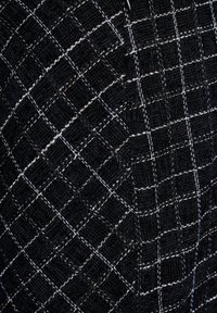 Schwarzer Textilstoff mit einem geometrischen Karomuster, das durch weiße Nähte akzentuiert wird und ein strukturiertes Erscheinungsbild erzeugt.