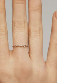 Delicada anilla de banda delgada con pequeños diamantes dispuestos en un sutil patrón de ondulación, llevada en el dedo medio.