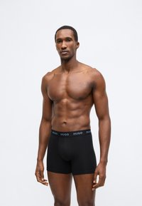 Cuecas boxer pretas de tecido macio, com uma cintura elástica que apresenta um logótipo em contraste. O design inclui um corte ajustado e comprimento até a metade da coxa.