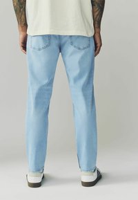 Jeans azzurri chiari con un design a gamba dritta, cinque tasche e vita media, abbinati a sneaker bianche con strisce nere.