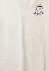 Valkoinen puuvillainen t-paita, jossa on yksinkertainen musta kuva kahvikupista lautasella lusikan kanssa, merkitty "kaffee".