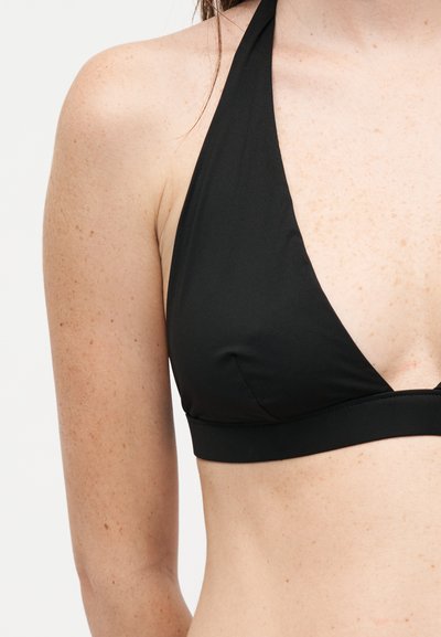 Γυναίκα με μαύρο μπικίνι τοπ halter, που δείχνει τους ώμους και το πάνω μέρος του κορμού με ανοιχτόχρωμο δέρμα και φακίδες.