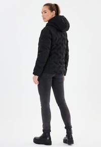 Svart puffjacka med huva, med en quiltad design. Bärs tillsammans med mörkgrå jeans och svarta ankelstövlar, vilket framhäver en avslappnad stil.