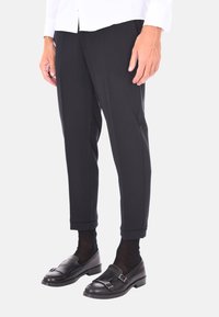 Pantaloni neri sartoriali con vestibilità a gamba dritta, caratterizzati da un tessuto liscio e orlo a fondo, abbinati a mocassini neri in pelle e calzini scuri.