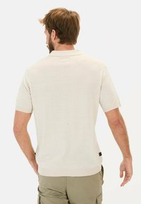 Beżowa koszulka polo z krótkim rękawem, z prążkowanym kołnierzykiem i dołem, o minimalistycznym designie i miękkiej fakturze, noszona z oliwkowymi szortami.