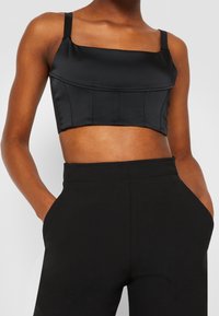 Top court en satin noir avec décolleté carré, fines bretelles et coutures structurées. Associé à un pantalon noir taille haute avec poches latérales.