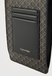 Η θήκη καρτών Calvin Klein από μαύρο δέρμα διαθέτει γεωμετρικό σχέδιο σε χρυσό. Περιλαμβάνει τέσσερις θήκες για κάρτες και ένα εμφανές λογότυπο. Λεπτή υφή.