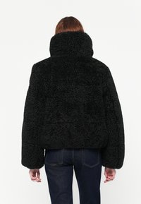 Zwarte fleecejack met een hoge kraag, oversize pasvorm en een gestructureerd oppervlak. Kenmerkt zich door gedropte schouders en lange mouwen.