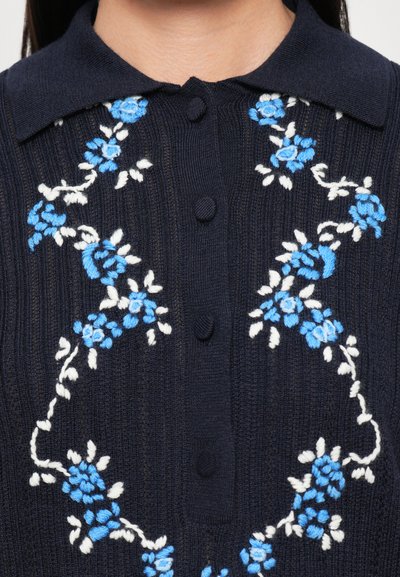 Cardigan tricotat bleumarin cu un design de broderie florală în culorile alb și albastru, având guler și închidere cu nasturi.