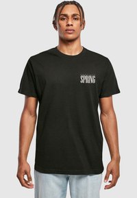 Sort bomulds T-shirt med rund halsudskæring, der har "Tropical SPRING" i fed hvid tekst øverst til venstre. Casual design, korte ærmer.