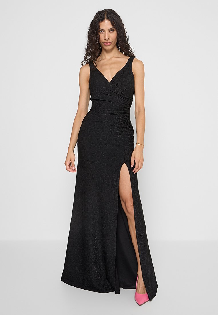 Czarna, błyszcząca suknia wieczorowa z dopasowaną górą, dekoltem w kształcie litery V i rozcięciem z boku. Posiada marszczoną konstrukcję i jest zestawiona z różowymi szpilkami.