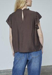 Brun, kortærmet top med rynkede ærmer og en nøglehulldetalje bagpå, parret med blå denim brede jeans. Glat stof struktur.