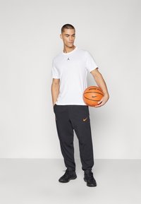 Bílý tričko s krátkým rukávem a černým logem Jordan, ve spojení s černými tepláky s oranžovým logem Nike a černými sportovními botami.