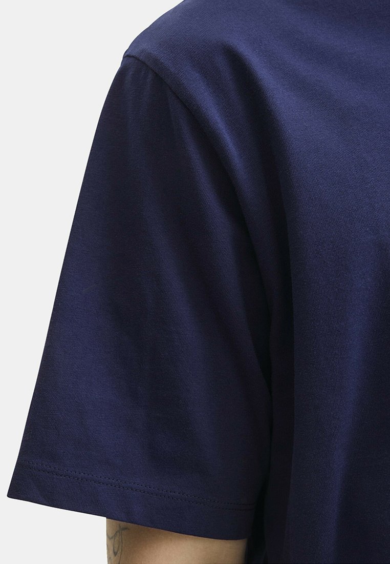 T-shirt en coton bleu marine à manches courtes, présentant une texture lisse et une coupe décontractée. Coutures latérales visibles le long de l'ourlet.
