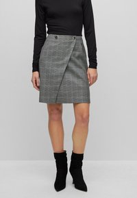 Grijze geruite rok met een wikkelontwerp, twee knopen aan de voorkant en een zoom boven de knie, gecombineerd met zwarte enkellaarsjes.