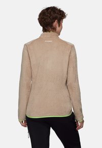 Veste en polaire beige avec un motif de diamants texturé, dotée d'un col haut et d'une bordure vert fluo le long de l'ourlet et des poignets. Logo de la marque à l'arrière.