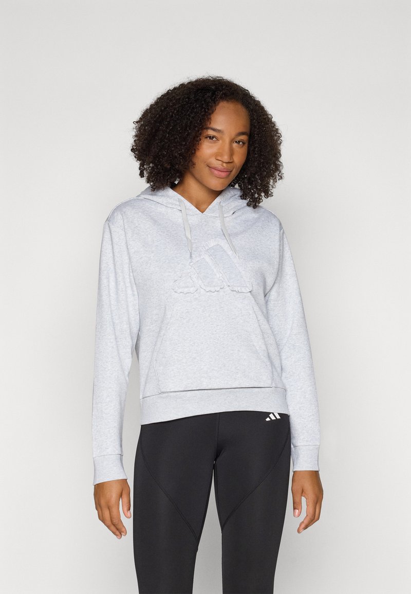 Lichtgrijze hoodie met een gerimpeld logo aan de voorkant, een capuchon met trekkoord en geribbelde manchetten. Gecombineerd met zwarte leggings met een subtiel logo.