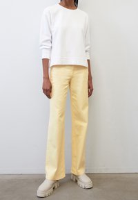 Felpa bianca con spalle drop, abbinata a jeans gialli a gamba larga e stivali con suola spessa color crema. Design semplice e pulito.