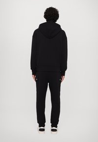 Sudadera negra con capucha y puños acanalados, combinada con pantalones de chándal negros que tienen bolsillos laterales. Tejido suave y corte relajado.